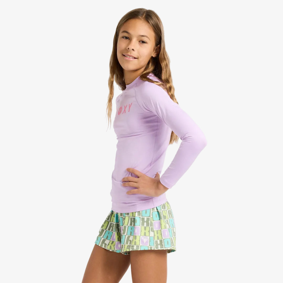 Young girl wearing a purple long-sleeve shirt and patterned shorts on a white background